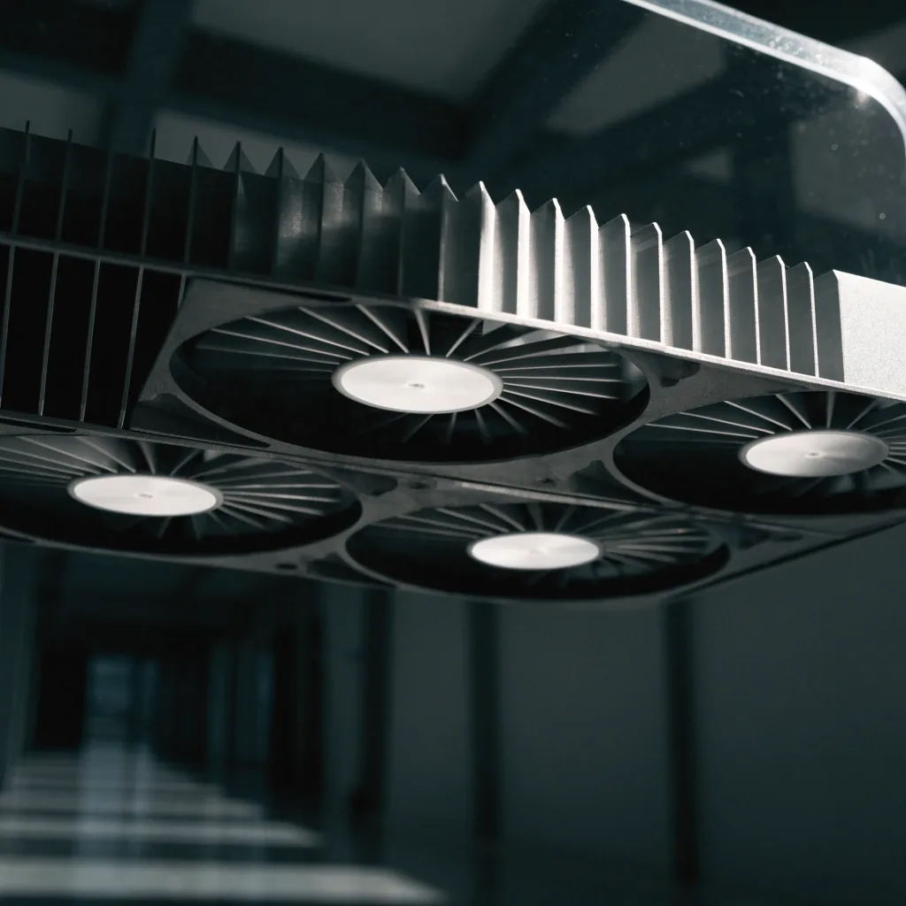 Triple-fan graphics card shroud angled under hard noon light on an acrylic shelf, dark hall falling away behind it